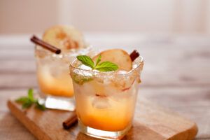 A glass of aromatic apple cider cocktail garnished with cinnamon sticks and fresh apple slices, evoking the essence of traditional autumn.