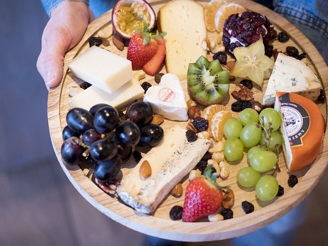 An inviting cheese and fruit tray featuring a variety of cheeses, grapes, strawberries, and slices of pear, elegantly displayed on a wooden board.