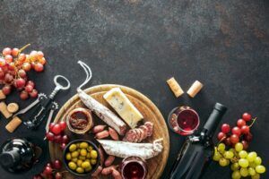 A beautifully arranged grazing spread featuring a bottle of red wine, assorted cheeses, cured meats, fresh fruits, nuts, and artisanal bread, set on a rustic wooden table.